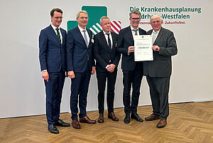 Übergabe in der Staatskanzlei: NRW-Ministerpräsident Hendrik Wüst (1.v.l.) und NRW-Gesundheitsminister Karl-Josef Laumann (4.v.l) überreichen den Förderbescheid an Dr. Matthias Ernst (2.v.l.), Univ.-Prof. Dr. Thomas Vordemvenne (Ärztlicher Direktor des EvKB) und an Thorsten Kaatze (3.v.l.). Foto: EvKB