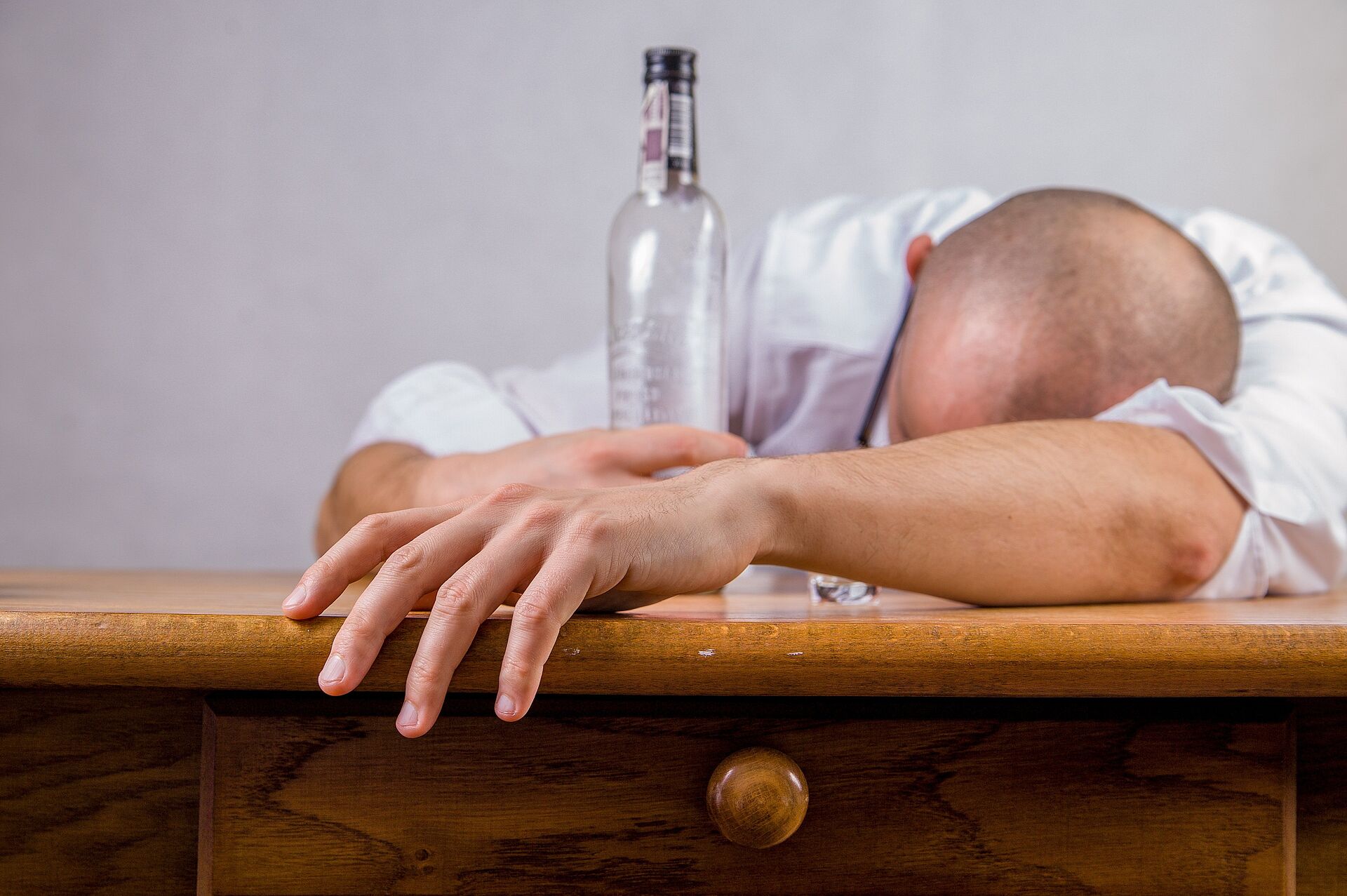 Ein Mann liegt mit dem Kopf auf einem Tisch. In der rechten Hand hält er eine Flasche.