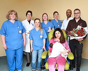 Mama Oula und Papa Mahmoud (rechts) können schon mit ihrer kleinen Julia kuscheln, dank der Teamarbeit im Perinatalzentrum: Pflegerische Leitung der Frauenklinik Susanne Auster, Prof. Dr. med. Constanze Banz-Jansen, Leitende Hebamme Nina Stahlschmidt, Hebamme Robine Schley, Fachgesundheits- und Kinderkrankenpflegerin Lisa Riepe und Univ.-Prof. Dr. med. Daniel Klotz, Leitender Arzt Neonatologie und Pädiatrische Intensivmedizin (v.l.n.r.).