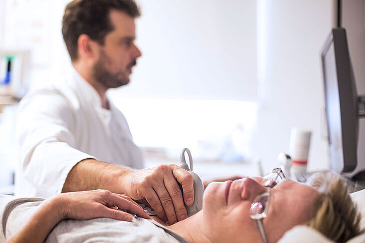 Ein Arzt führt an einer Patientin eine Ultraschall-Untersuchung der Halsschlagadern durch.