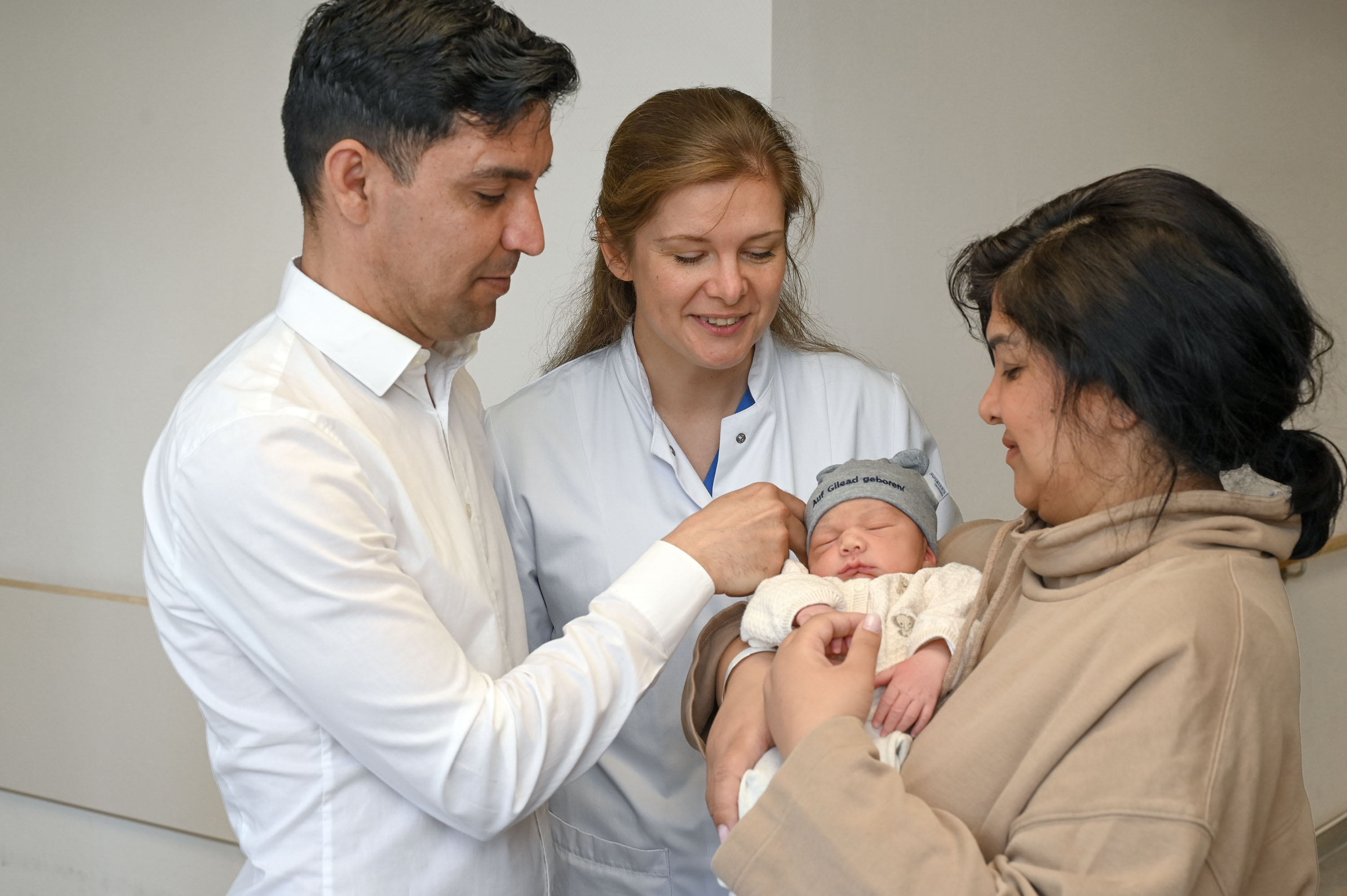 Ein Paar steh zusammen mit einer Ärztin auf dem Flur. Der Mann hält das neugeborene Baby auf dem Arm.